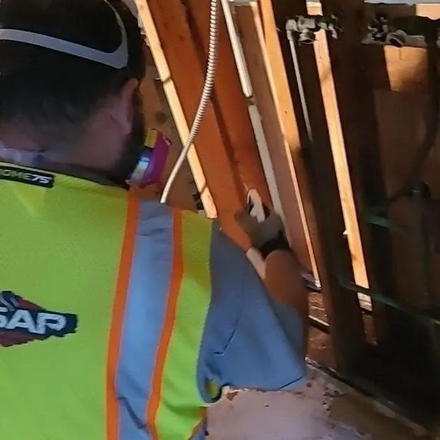 ASAP technician in a safety vest and respirator cleaning wall framing